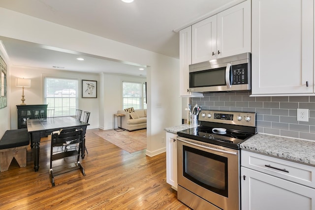 kitchen featuring stainless steel appliances, tasteful backsplash, white cabinetry, light stone countertops, and light wood-type flooring