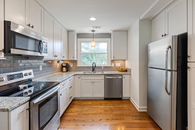 kitchen with light stone counters, a sink, appliances with stainless steel finishes, decorative backsplash, and light wood finished floors