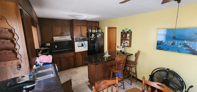 kitchen featuring white oven, dark countertops, black refrigerator with ice dispenser, a sink, and a peninsula