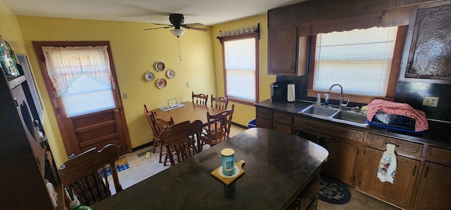 kitchen with ceiling fan, dark brown cabinetry, a sink, baseboards, and dark countertops