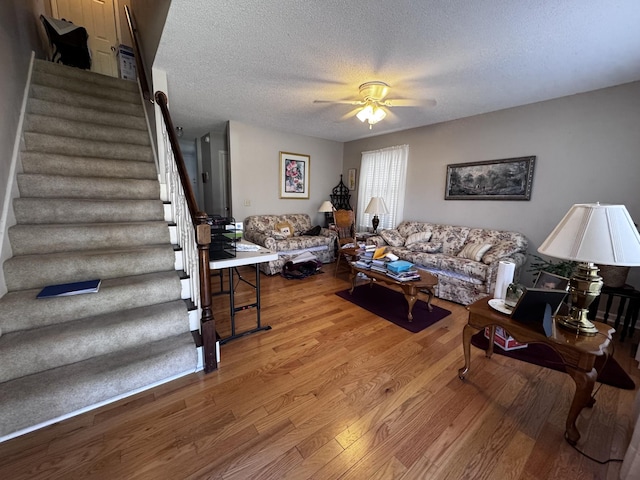 living area with wood finished floors, ceiling fan, a textured ceiling, and stairs