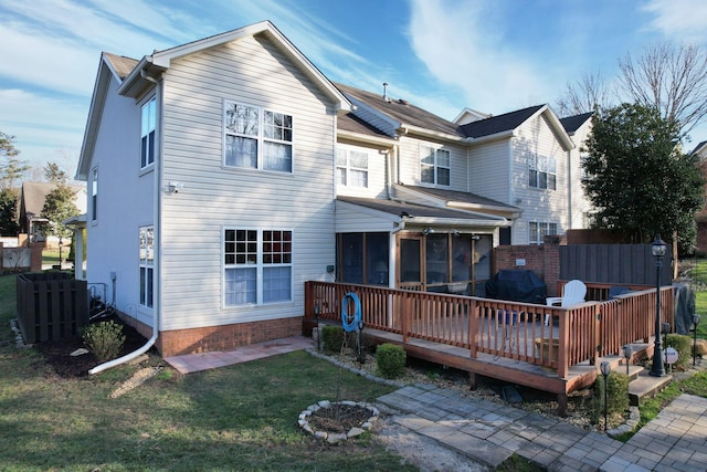 back of property featuring a wooden deck, a lawn, fence, and a sunroom