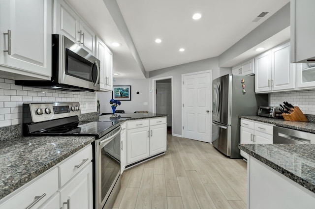 kitchen with white cabinets, light wood finished floors, stainless steel appliances, and dark stone countertops