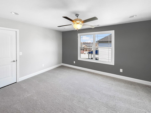 carpeted spare room with visible vents, baseboards, and a ceiling fan