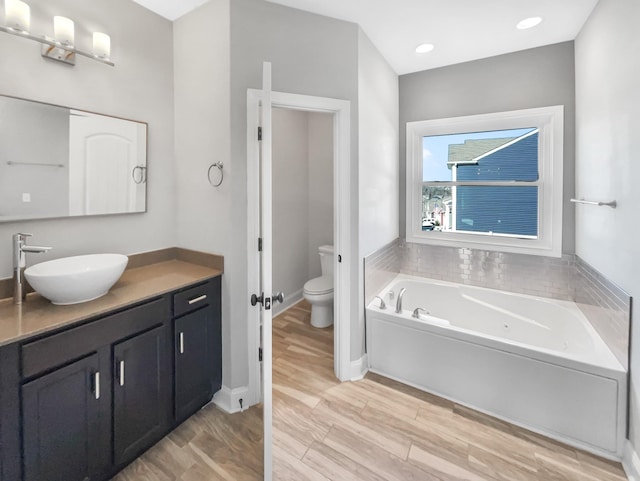 bathroom featuring toilet, vanity, wood finished floors, baseboards, and a bath