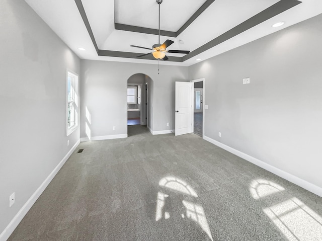 unfurnished bedroom featuring arched walkways, a raised ceiling, visible vents, carpet flooring, and baseboards