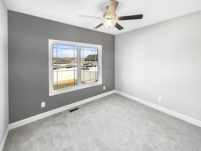 carpeted spare room featuring a ceiling fan, visible vents, and baseboards