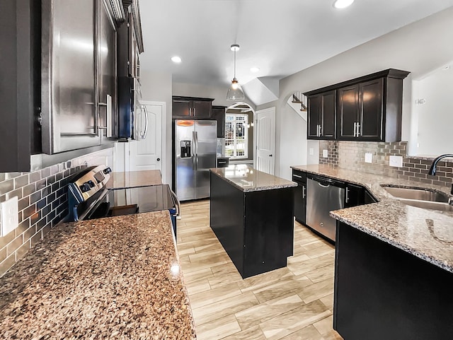 kitchen with a kitchen island, light stone counters, a sink, stainless steel appliances, and backsplash