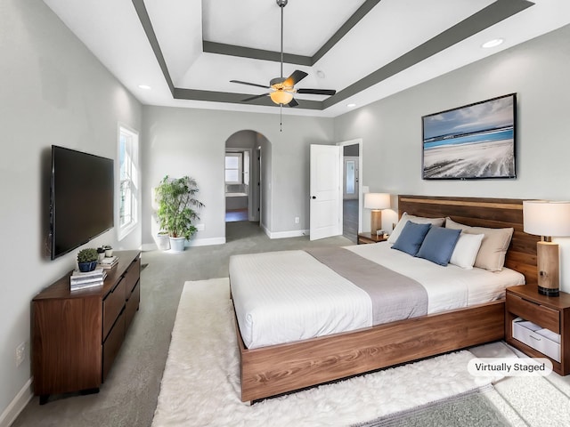 bedroom with baseboards, arched walkways, a tray ceiling, carpet floors, and recessed lighting