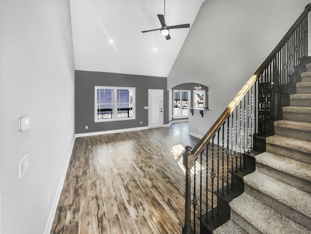 unfurnished living room with arched walkways, high vaulted ceiling, wood finished floors, a ceiling fan, and baseboards