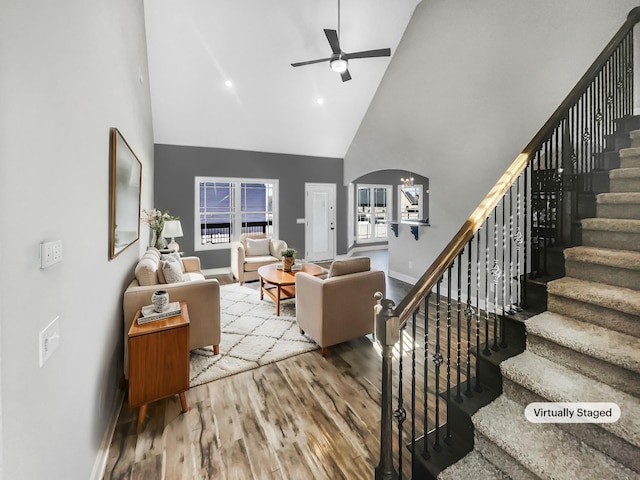 living area featuring arched walkways, a ceiling fan, wood finished floors, high vaulted ceiling, and baseboards