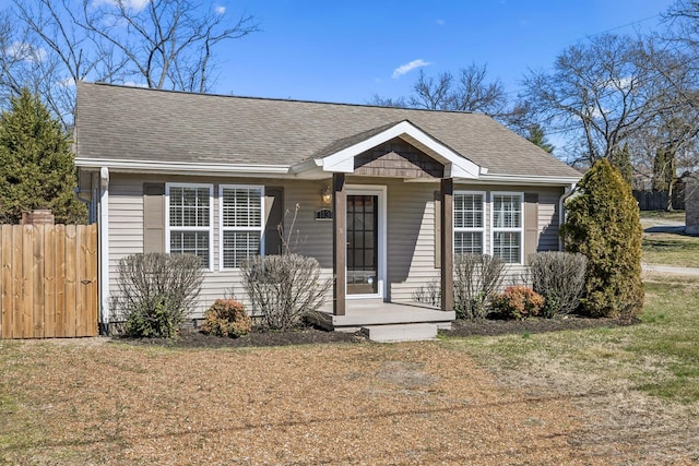 bungalow-style home featuring covered porch, fence, and roof with shingles