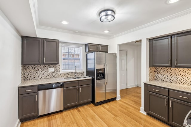 kitchen with light wood finished floors, decorative backsplash, appliances with stainless steel finishes, ornamental molding, and a sink