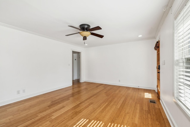 spare room with light wood finished floors, visible vents, ornamental molding, a ceiling fan, and baseboards