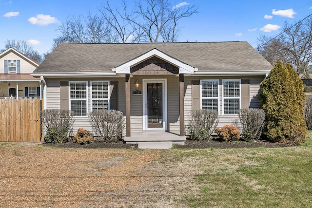 bungalow-style home featuring fence, a front lawn, and roof with shingles