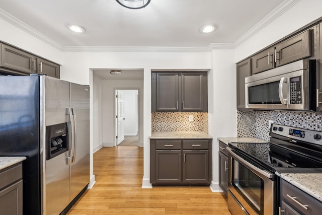 kitchen featuring light stone countertops, light wood-style floors, ornamental molding, appliances with stainless steel finishes, and decorative backsplash