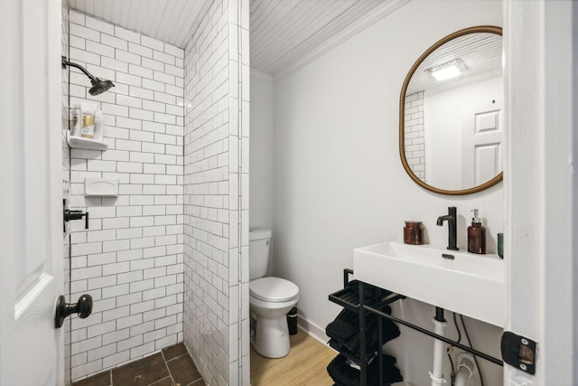 bathroom with crown molding, toilet, a sink, wood finished floors, and tiled shower