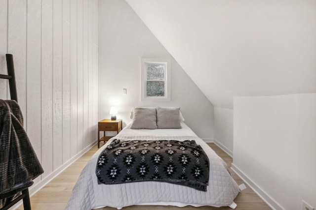 bedroom with lofted ceiling, light wood-style flooring, and baseboards