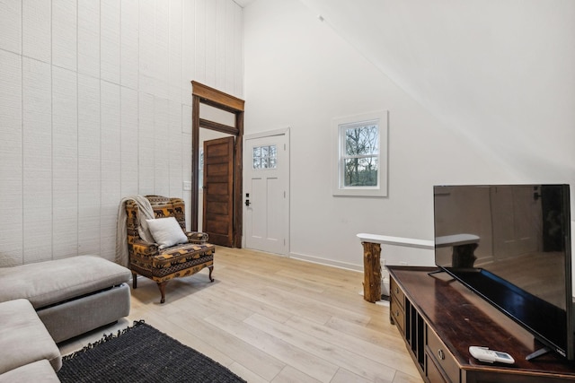 living area with high vaulted ceiling, light wood-type flooring, and baseboards