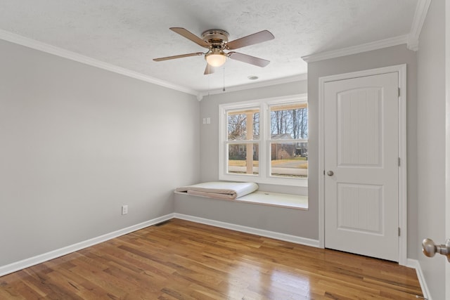 empty room featuring a textured ceiling, ornamental molding, wood finished floors, and baseboards