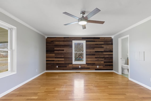 spare room with baseboards, an accent wall, light wood finished floors, and wooden walls