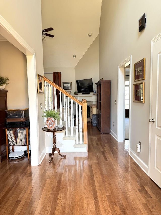 stairway featuring baseboards, a high ceiling, hardwood / wood-style floors, and a ceiling fan