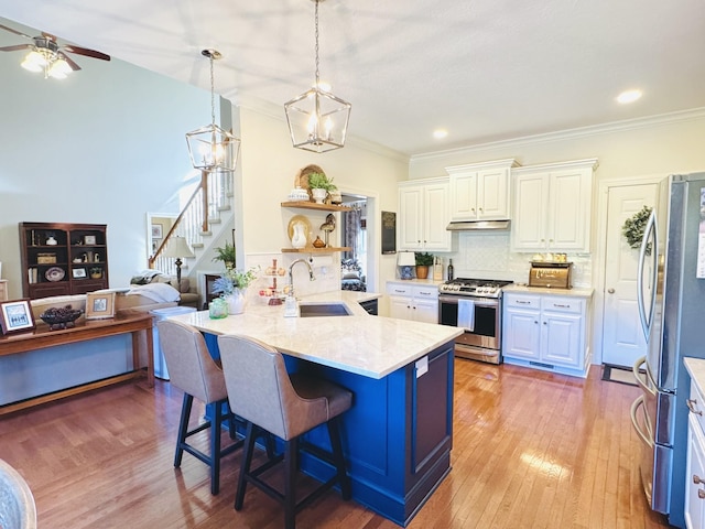 kitchen featuring open shelves, a sink, white cabinets, appliances with stainless steel finishes, and a kitchen bar