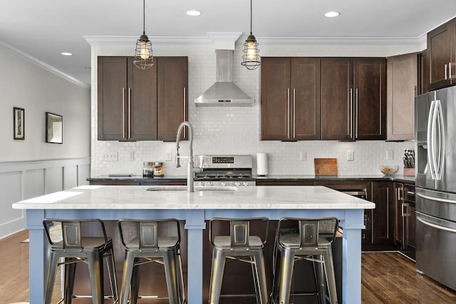 kitchen featuring a breakfast bar, stainless steel appliances, dark wood-type flooring, ornamental molding, and wall chimney exhaust hood