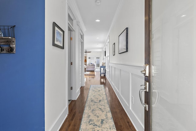 hallway featuring dark wood-type flooring, crown molding, and a decorative wall