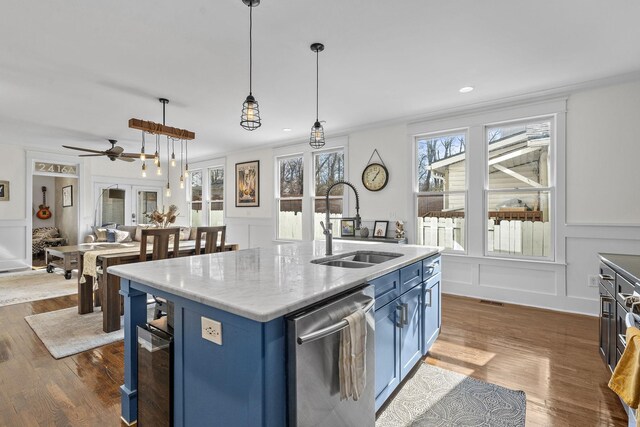 kitchen featuring blue cabinetry, a sink, stainless steel dishwasher, and a decorative wall