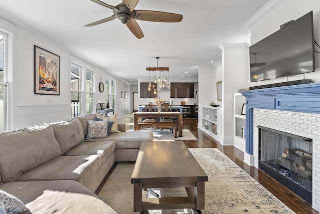 living area featuring a warm lit fireplace, a decorative wall, ornamental molding, wainscoting, and dark wood finished floors