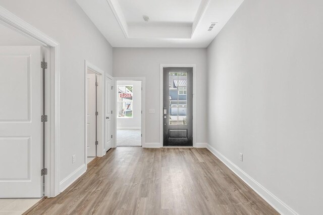 entrance foyer featuring a tray ceiling, wood finished floors, visible vents, and baseboards