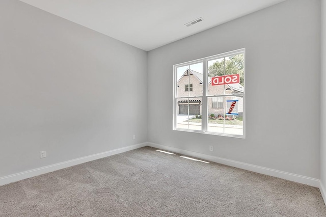 carpeted spare room featuring plenty of natural light, visible vents, and baseboards