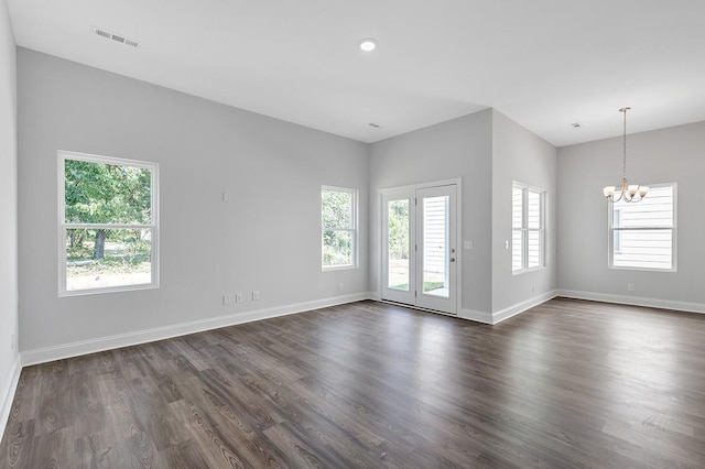 spare room with a chandelier, dark wood-type flooring, a wealth of natural light, and baseboards