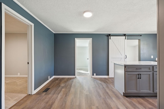 spare room with ornamental molding, a barn door, wood finished floors, and visible vents