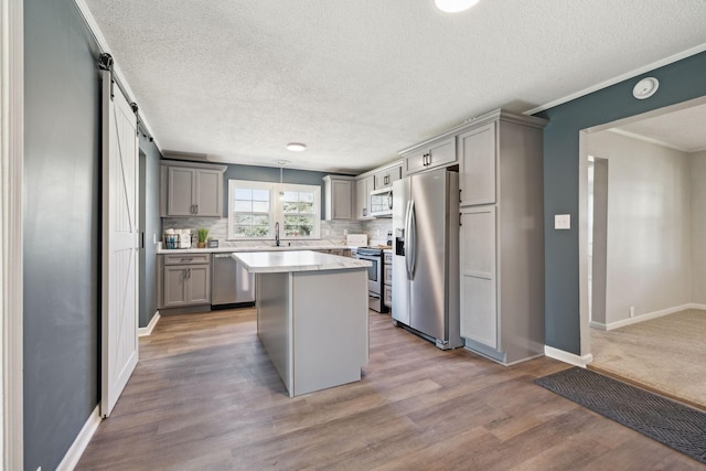 kitchen with stainless steel appliances, tasteful backsplash, light countertops, gray cabinetry, and a barn door