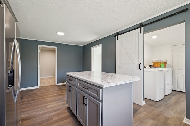 kitchen featuring a barn door, washing machine and dryer, gray cabinetry, dark wood-type flooring, and stainless steel refrigerator with ice dispenser