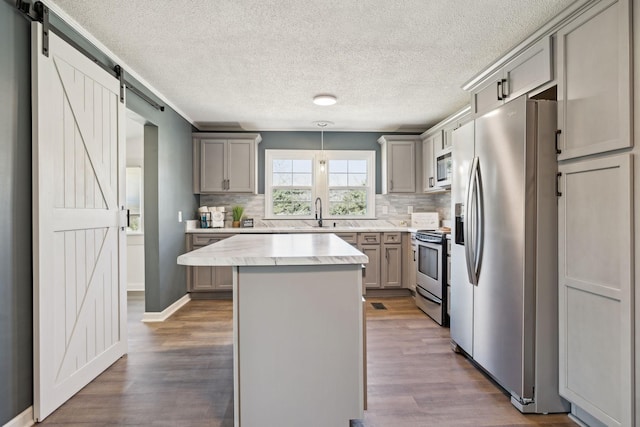 kitchen with a center island, gray cabinetry, a barn door, appliances with stainless steel finishes, and wood finished floors