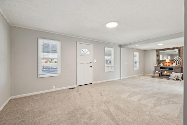 entrance foyer featuring carpet flooring, visible vents, baseboards, a glass covered fireplace, and crown molding