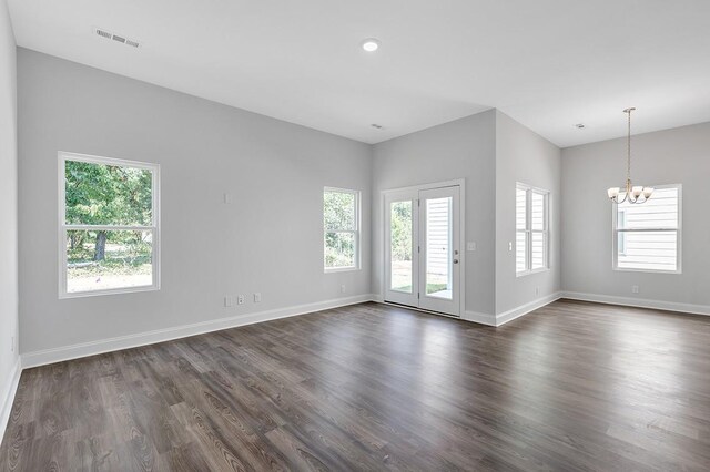 spare room featuring a wealth of natural light, a notable chandelier, baseboards, and dark wood-type flooring