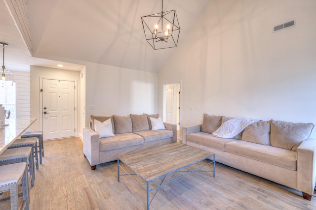 living area with high vaulted ceiling, light wood-style flooring, visible vents, and a chandelier