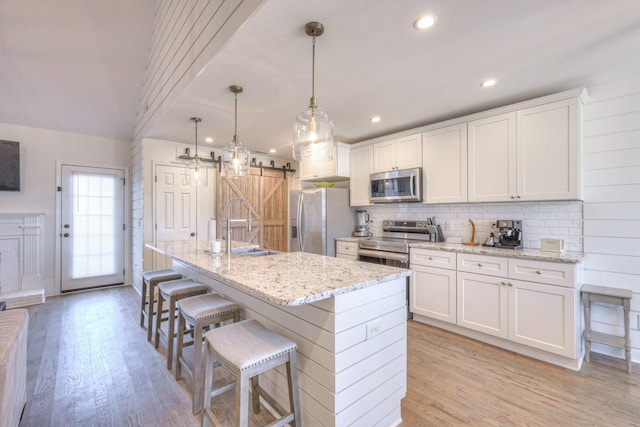 kitchen with a barn door, appliances with stainless steel finishes, light wood-style flooring, and a sink