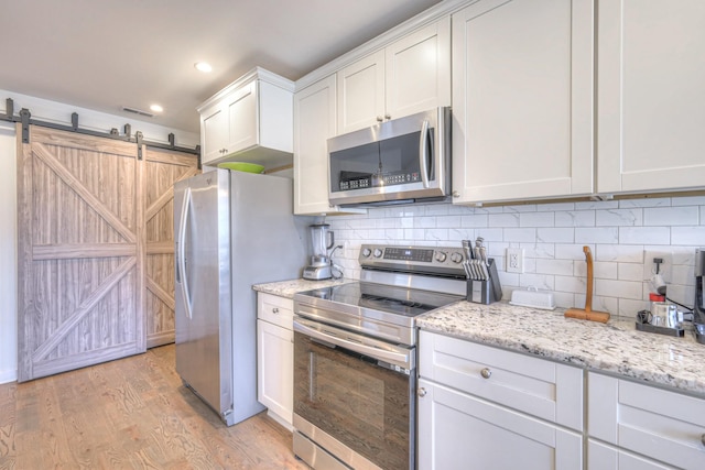 kitchen with tasteful backsplash, appliances with stainless steel finishes, white cabinetry, light stone countertops, and light wood-type flooring