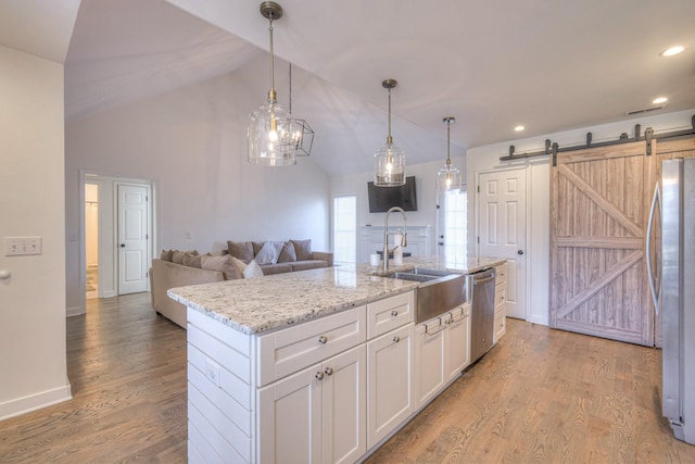 kitchen featuring a barn door, light wood-style flooring, stainless steel appliances, a sink, and white cabinetry