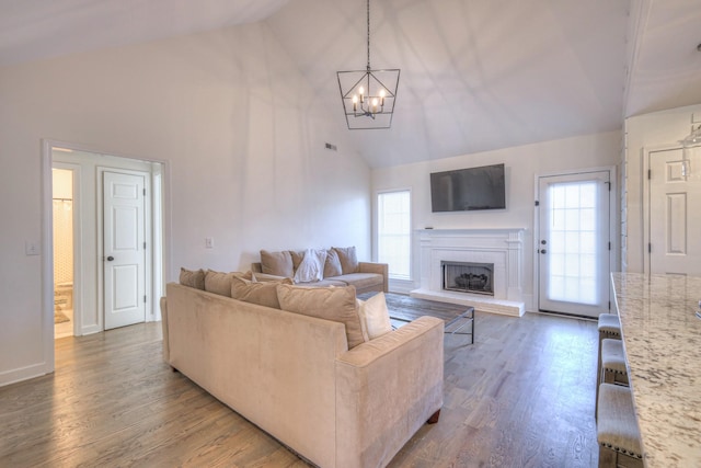 living area with a chandelier, high vaulted ceiling, a fireplace with raised hearth, wood finished floors, and baseboards