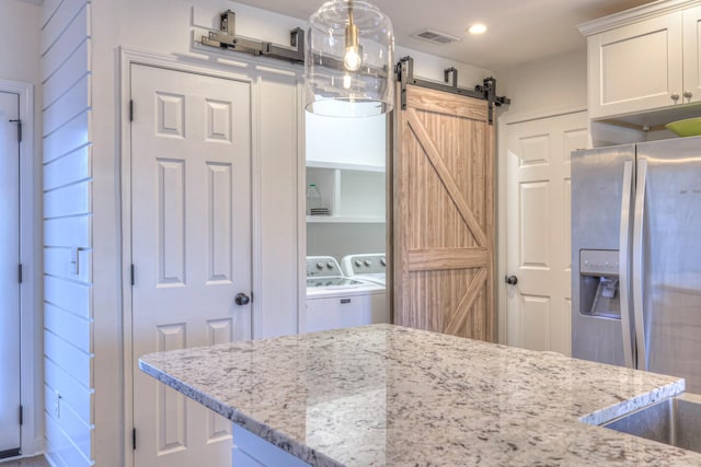 kitchen with a barn door, washer and clothes dryer, light stone countertops, white cabinetry, and stainless steel refrigerator with ice dispenser