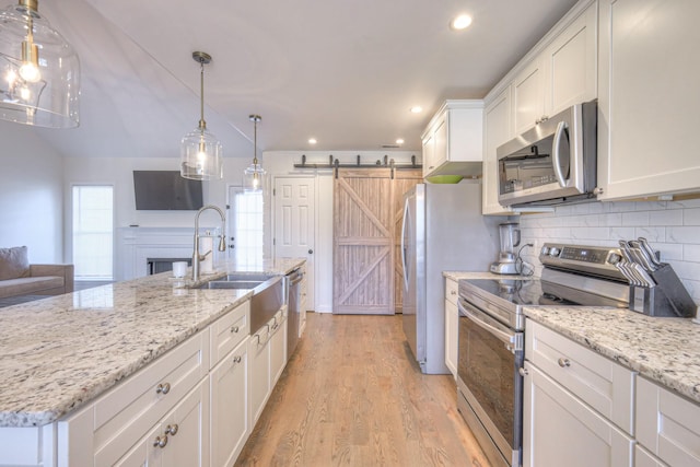 kitchen featuring stainless steel appliances, a barn door, white cabinetry, a sink, and light wood-type flooring