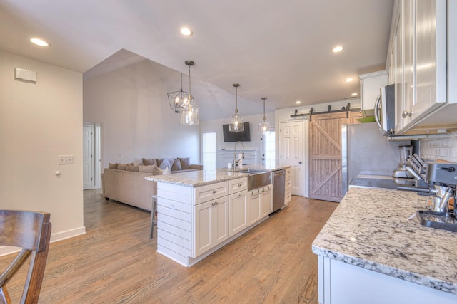 kitchen featuring a barn door, light wood-style flooring, appliances with stainless steel finishes, white cabinetry, and a sink