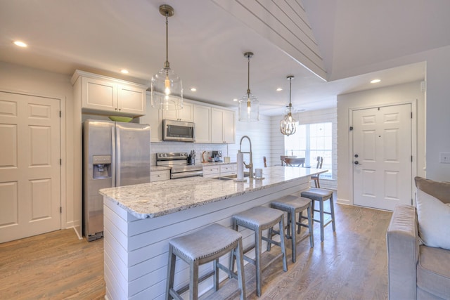 kitchen featuring light wood finished floors, white cabinets, decorative backsplash, appliances with stainless steel finishes, and a kitchen breakfast bar