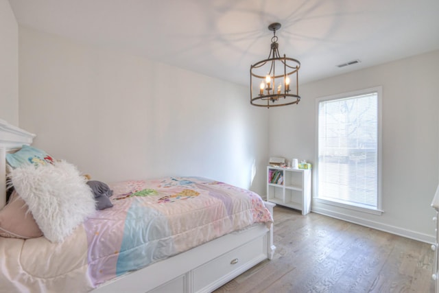 bedroom with light wood-style floors, visible vents, baseboards, and an inviting chandelier